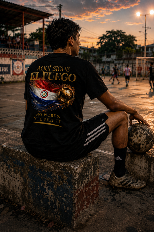 Aquí Sigue El Fuego Tee | Gold Soccer & Paraguay Flag Design | Bilingual Edition | Back Print